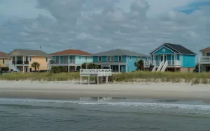 A view of colorful beachfront homes elevated on stilts along the sandy shore of New Smyrna Beach, Florida, representing the coastal communities where GRIT Roofing provides expert local roofing services.